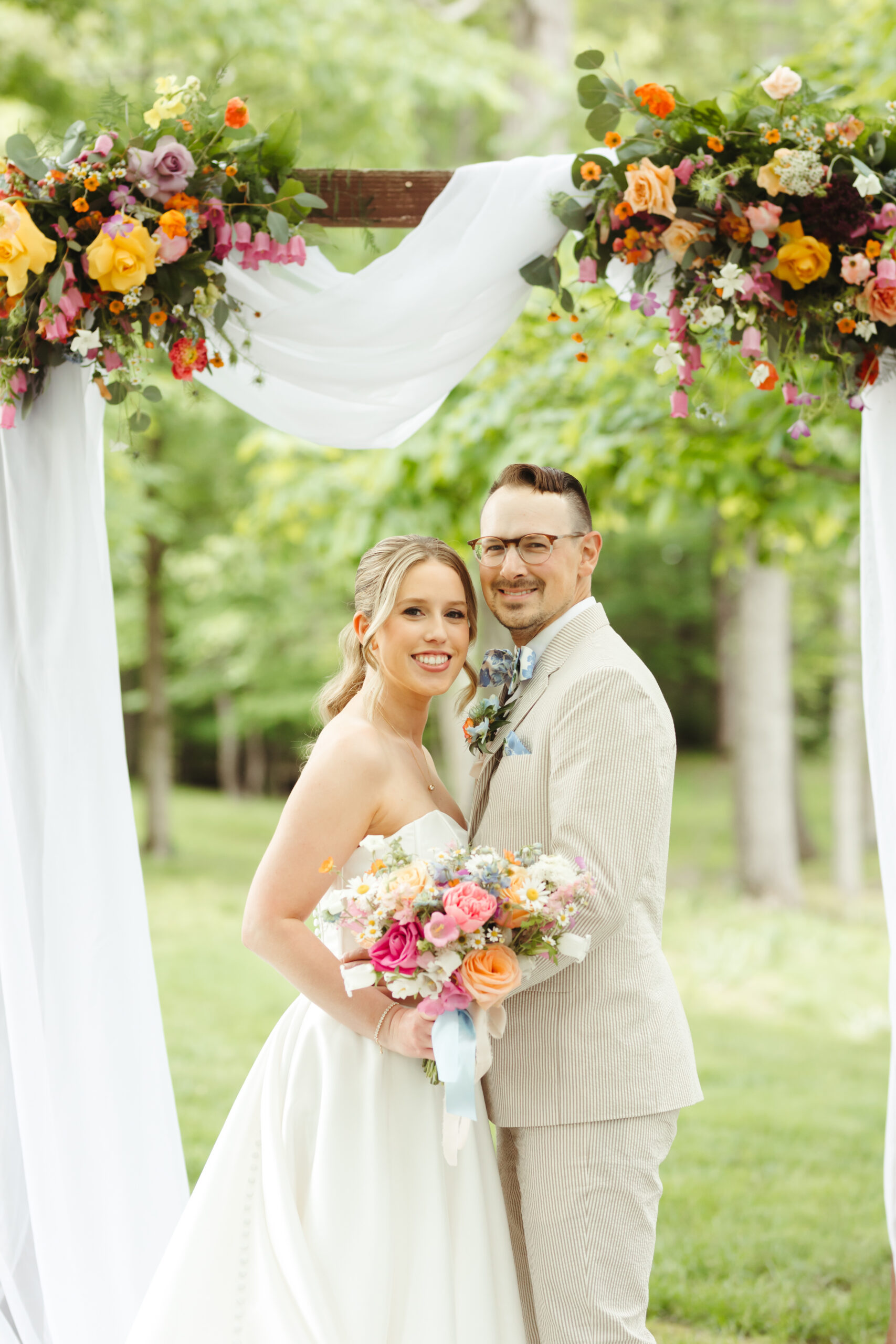 bride and groom smiling under their ceremony arch filled with flowers.